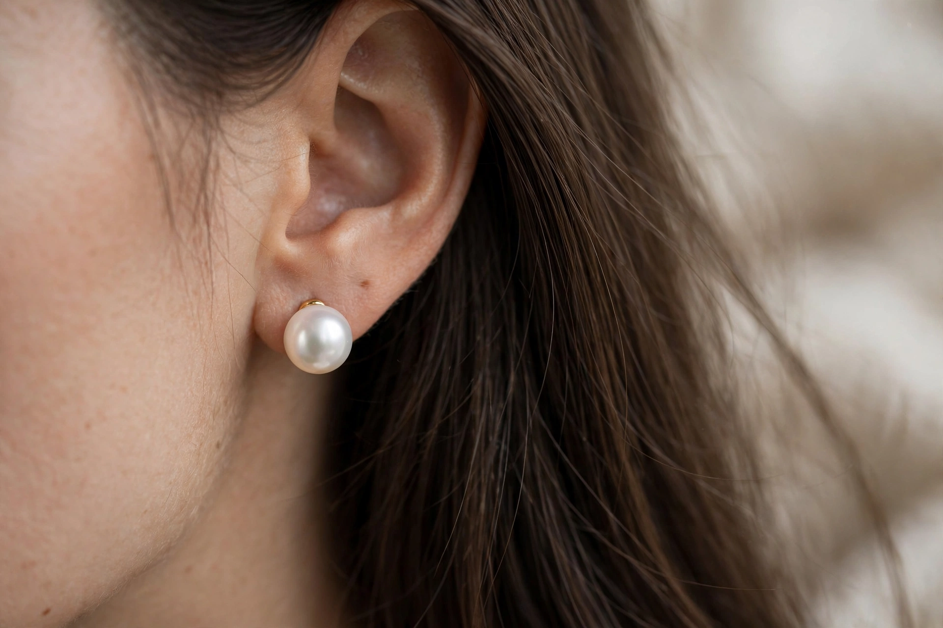 Close-up of elegant round pearl stud earrings worn by a woman with long straight hair