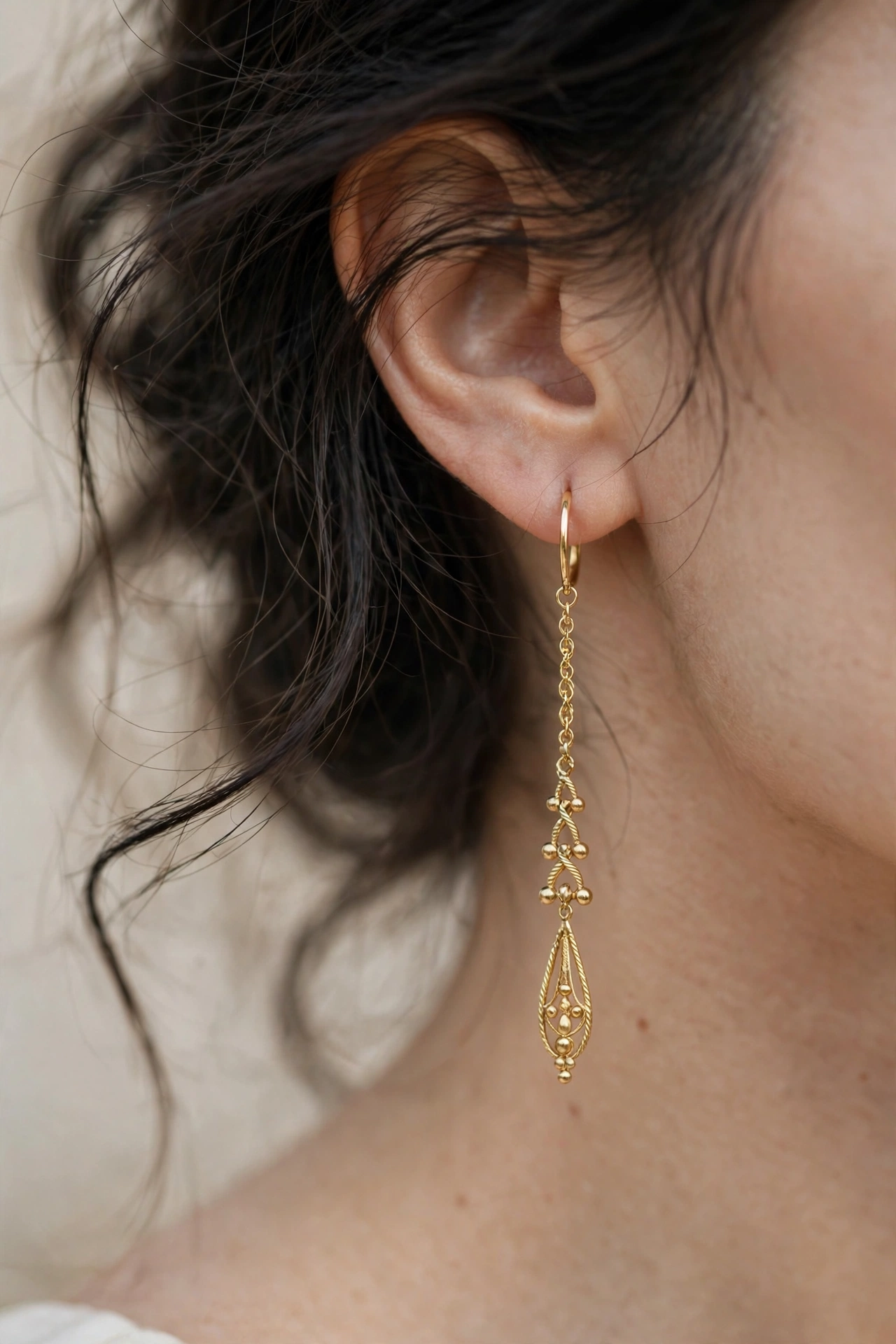 Close-up of elegant long gold drop earrings worn by a woman with soft dark hair